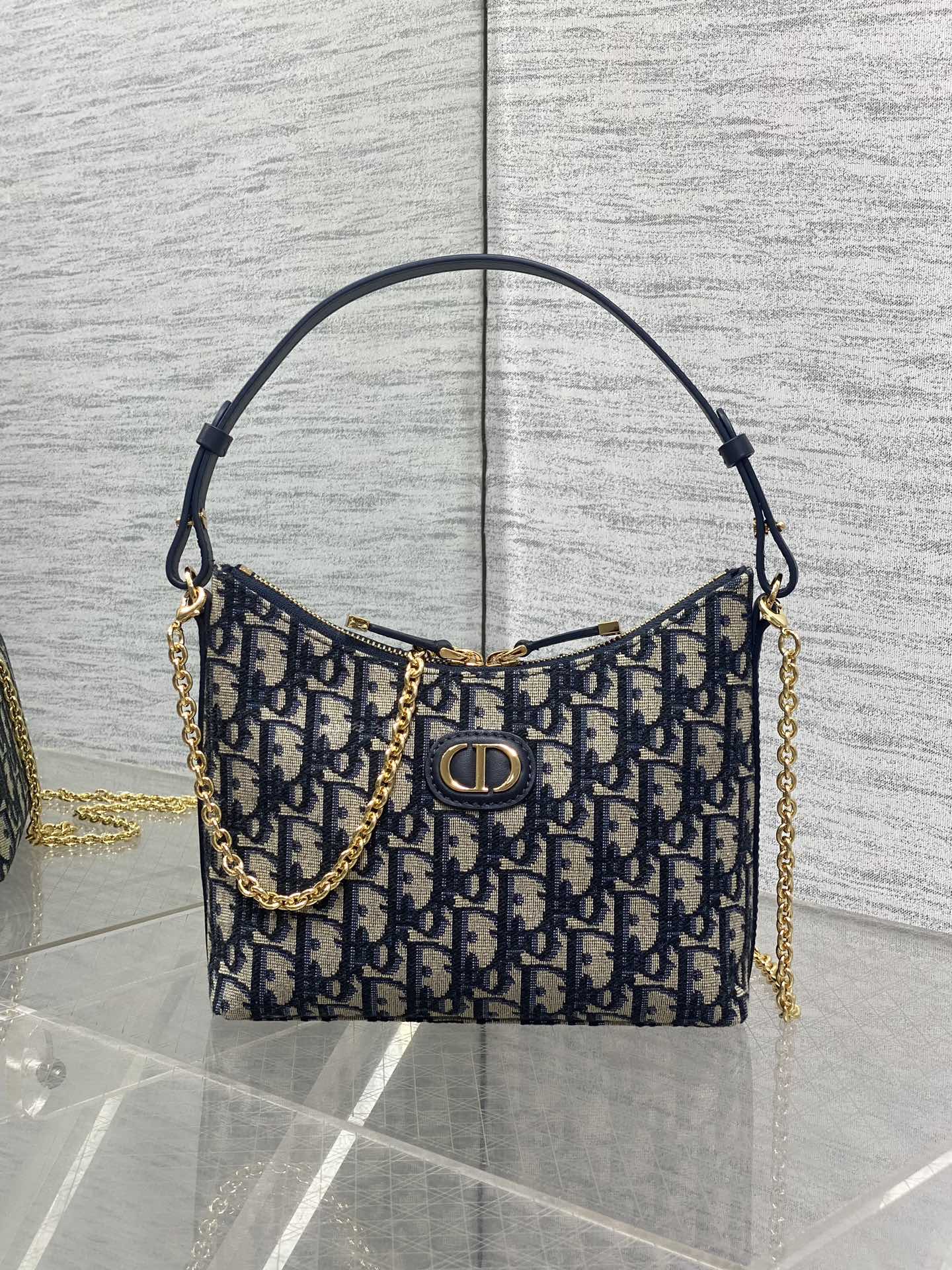 Designer handbag with gold chain and patterned fabric on a reflective surface